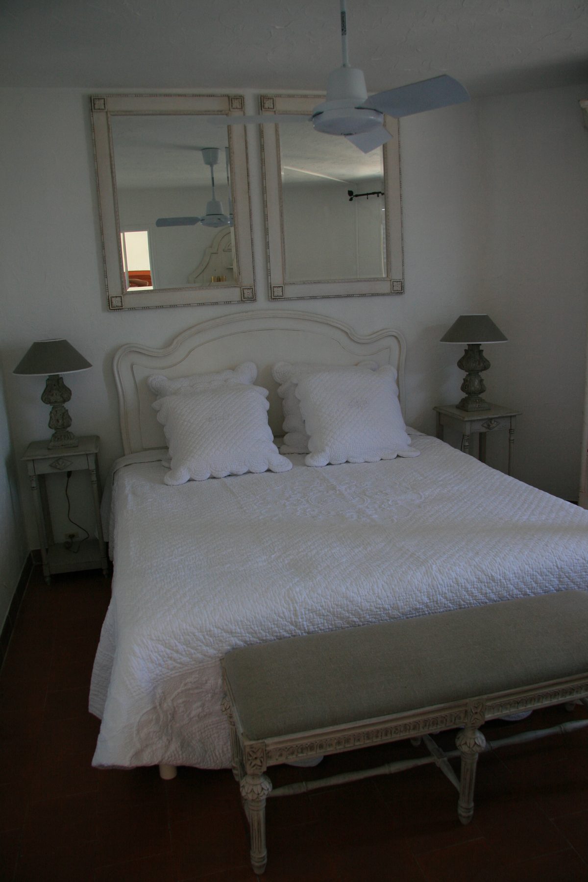Master bedroom with made-up king bed, twin mirrors and ceiling fan