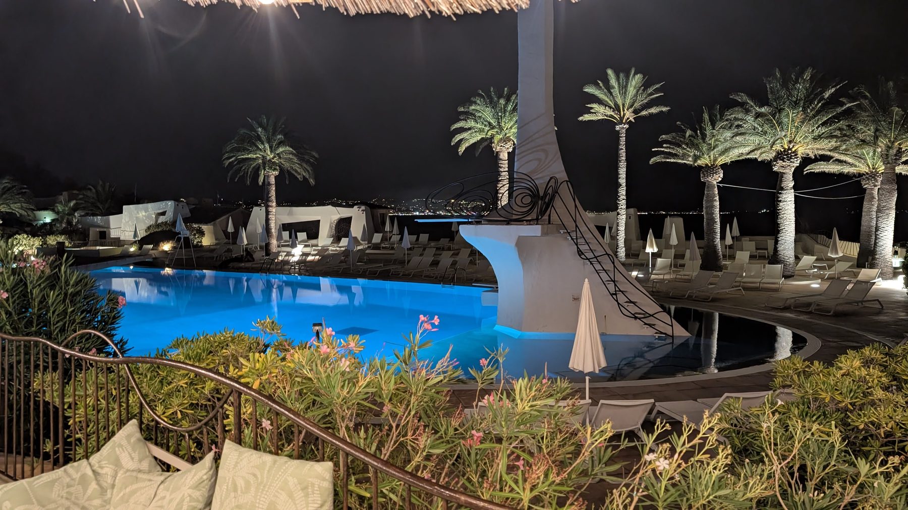 Summer Club pool lit at night with palms and diving tower